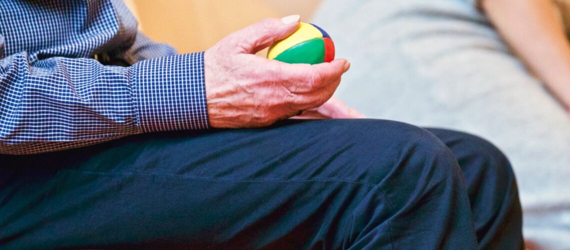 Elderly man holding a colorful therapy ball indoors, promoting relaxation and health.