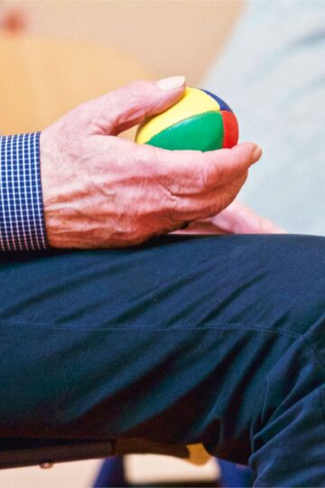 Elderly man holding a colorful therapy ball indoors, promoting relaxation and health.
