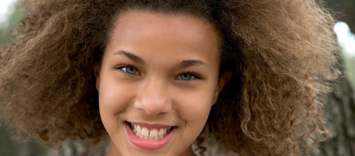A smiling teenager with beautiful natural curls enjoying the day outdoors, embodying vibrant youthfulness.