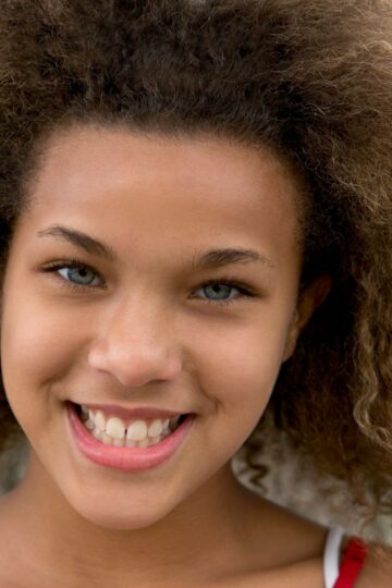 A smiling teenager with beautiful natural curls enjoying the day outdoors, embodying vibrant youthfulness.