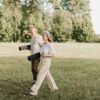 Elderly couple walking on grass carrying yoga mats, enjoying a sunny day outdoors.