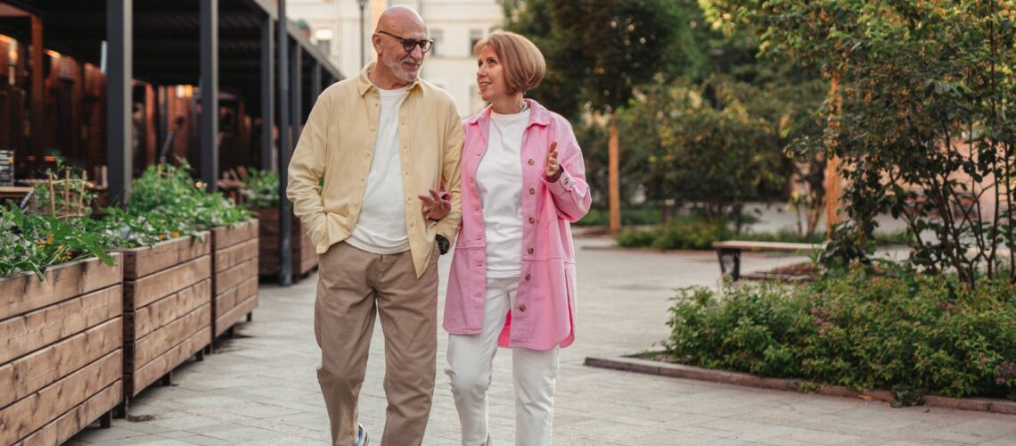 Happy senior couple walking together in a lush outdoor urban setting.