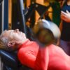 Elderly man exercising with a barbell at the gym under supervision.