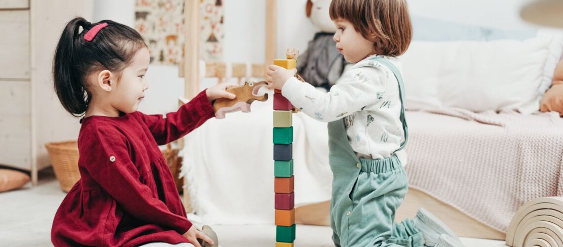 Two children playing and building with colorful wooden toys indoors.