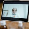 Elderly male doctor in white coat on a digital tablet screen during a virtual medical consultation.
