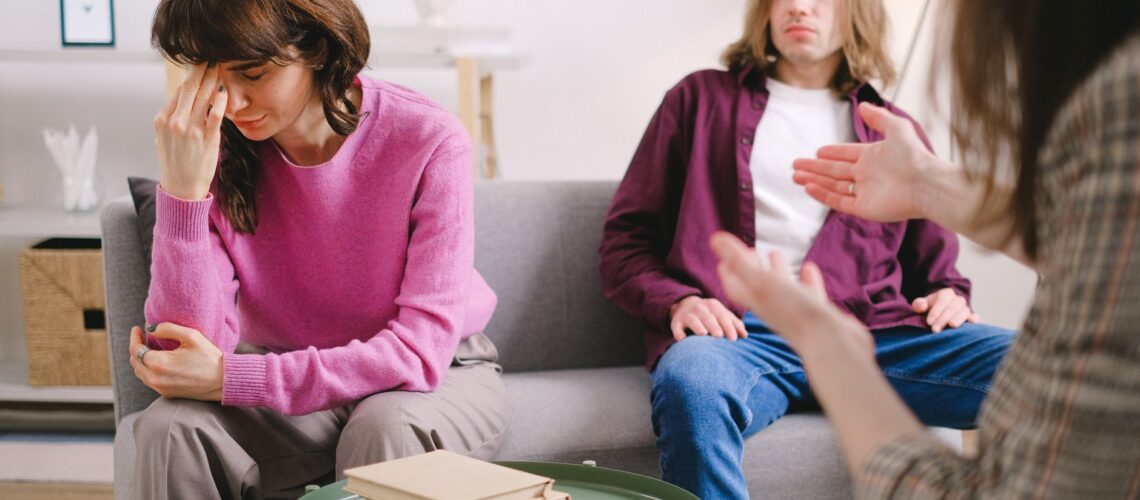 A couple undergoing therapy, expressing emotions on a sofa in a counseling office.