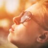Close-up portrait of a woman with sunglasses enjoying sunlight and relaxation outdoors.