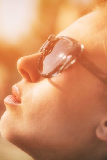 Close-up portrait of a woman with sunglasses enjoying sunlight and relaxation outdoors.