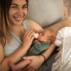 A mother lovingly feeds her newborn with a bottle while smiling at the camera.