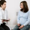 A pregnant woman consulting with a female doctor in a medical clinic setting.