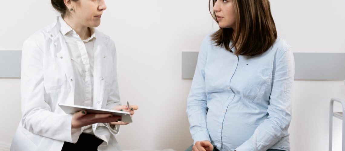 A pregnant woman consulting with a female doctor in a medical clinic setting.