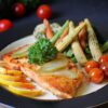 Colorful plate of grilled fish garnished with lemon, pickles, and fresh vegetables. Perfect for healthy meal inspiration.