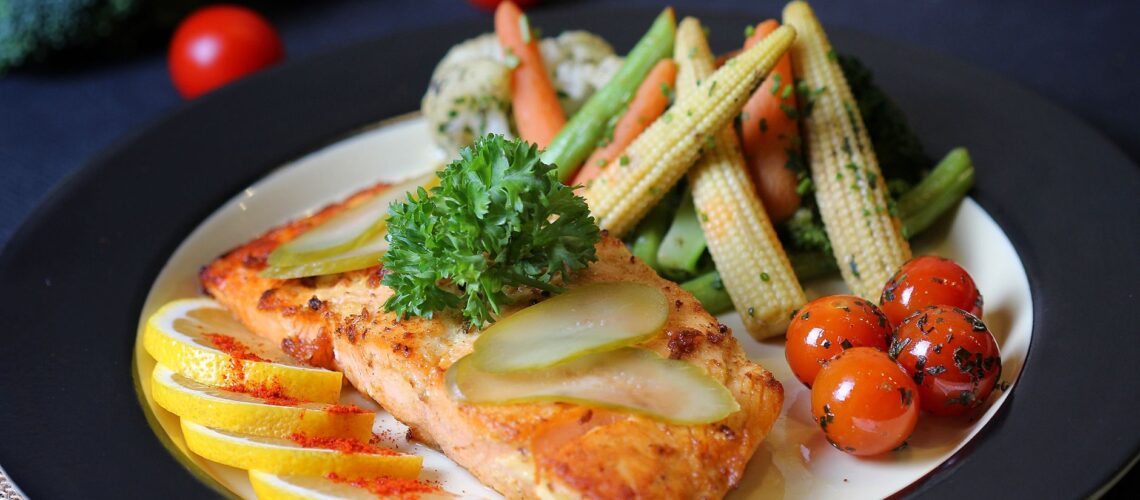 Colorful plate of grilled fish garnished with lemon, pickles, and fresh vegetables. Perfect for healthy meal inspiration.