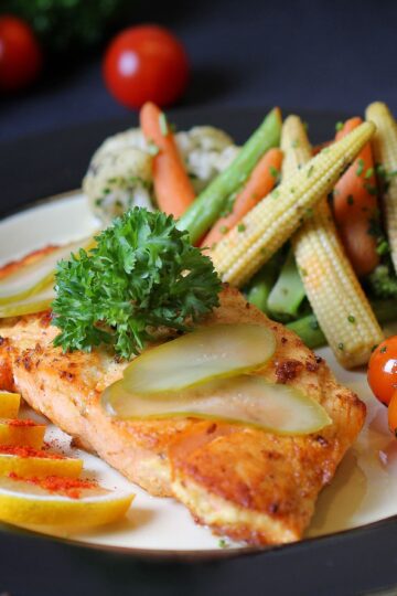 Colorful plate of grilled fish garnished with lemon, pickles, and fresh vegetables. Perfect for healthy meal inspiration.