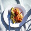 A vibrant meal of quinoa and vegetables served on a white plate with fork and shadows.