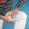 Close-up of a man's hands on his knee, showing pain or injury, on a blue background.