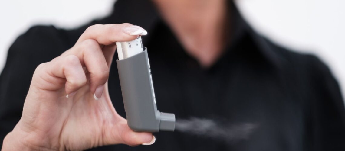 Person holding and using an inhaler, showcasing healthcare and respiratory care indoors.