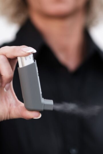 Person holding and using an inhaler, showcasing healthcare and respiratory care indoors.