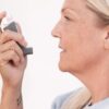 Middle-aged woman using an asthma inhaler to alleviate breathing difficulties.