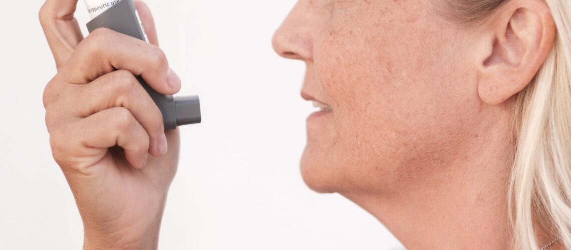 Middle-aged woman using an asthma inhaler to alleviate breathing difficulties.