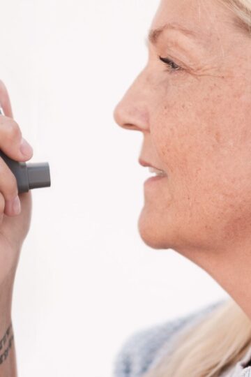 Middle-aged woman using an asthma inhaler to alleviate breathing difficulties.