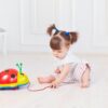 Cute toddler sits on the floor playing with a colorful toy ladybug.