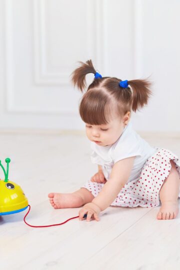 Cute toddler sits on the floor playing with a colorful toy ladybug.