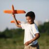 Young boy joyfully playing with a toy airplane outdoors on a sunny day.