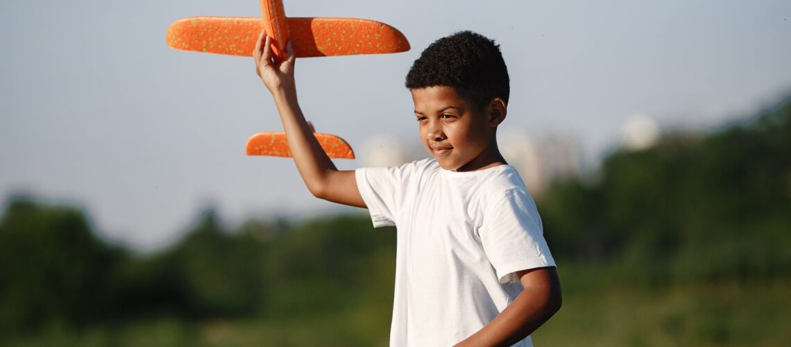 Young boy joyfully playing with a toy airplane outdoors on a sunny day.