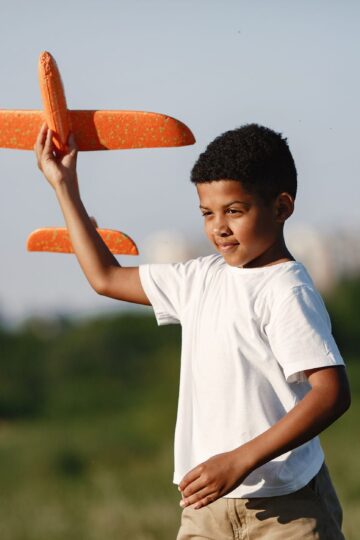 Young boy joyfully playing with a toy airplane outdoors on a sunny day.