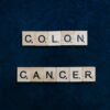 Wooden Scrabble tiles spelling 'Colon Cancer' on a blue background.