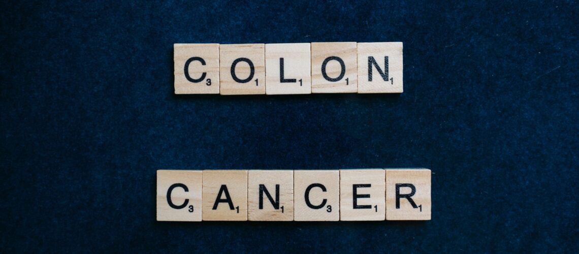 Wooden Scrabble tiles spelling 'Colon Cancer' on a blue background.