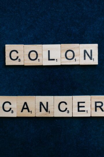 Wooden Scrabble tiles spelling 'Colon Cancer' on a blue background.