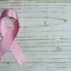 A pink ribbon symbolizing cancer awareness placed on a light wooden background.