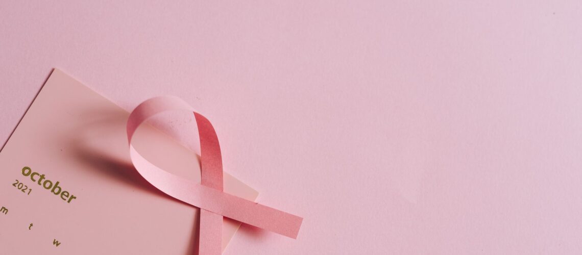 Breast cancer awareness concept with a pink ribbon on a pink October calendar.