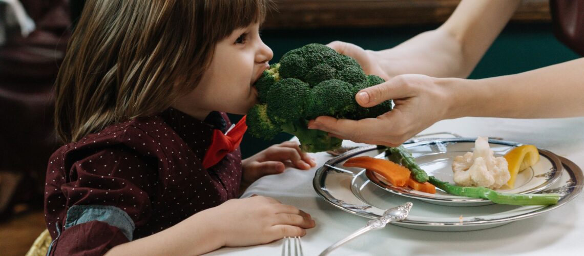 Cute child eating broccoli, promoting healthy eating habits indoors.