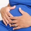 Closeup of a pregnant woman resting her hands on her belly, displaying a watch and a ring.
