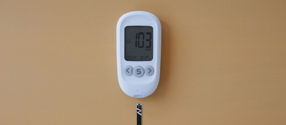 Close-up of a digital glucose meter displaying blood sugar level on a brown surface.