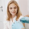 Blond woman in clinic receiving blood test with healthcare professional holding sample.