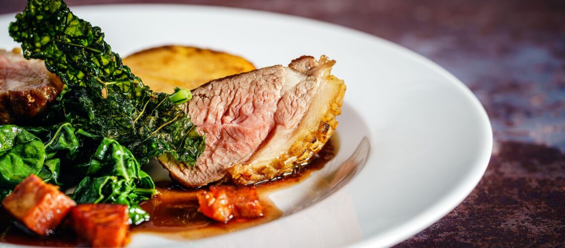 Savor a gourmet duck breast dish with crispy kale and a rich sauce, exquisitely presented on a white plate.
