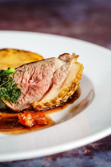Savor a gourmet duck breast dish with crispy kale and a rich sauce, exquisitely presented on a white plate.
