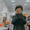 Young boy covers face in a bustling school classroom, indicating stress or anxiety.