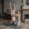 Pregnant woman doing yoga poses with a trainer in cozy indoor setting.