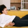 A pregnant woman comfortably rests on a yellow sofa at home, embodying warmth and tranquility.