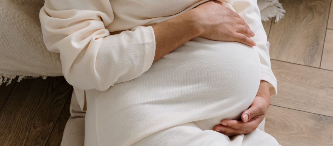 A serene moment of a pregnant woman in a cozy white dress holding her belly.
