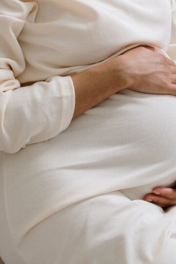 A serene moment of a pregnant woman in a cozy white dress holding her belly.