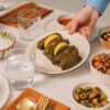 A Mediterranean dining setting with dolmas, salads, and a hand serving food.