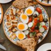 A vibrant Mediterranean breakfast featuring boiled eggs, grilled halloumi, and fresh vegetables on a beautifully patterned plate.