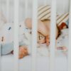 A baby peacefully sleeping with a pacifier in a cozy crib with plush blankets.