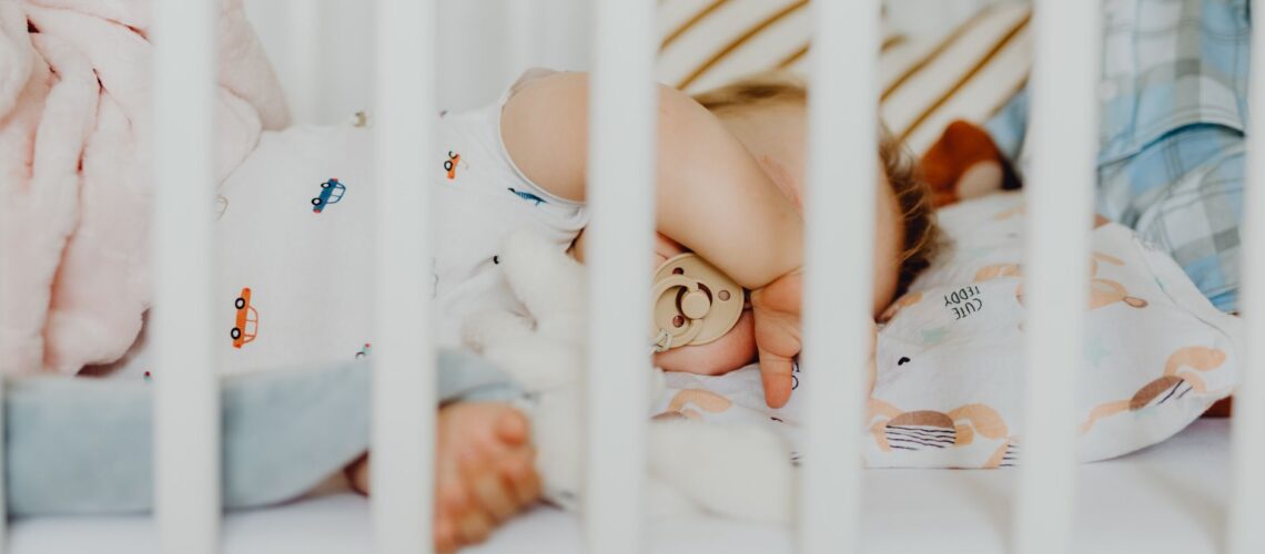 A baby peacefully sleeping with a pacifier in a cozy crib with plush blankets.